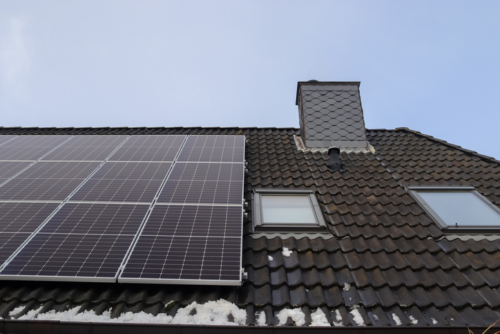 Solar panels producing clean energy on a roof of a residential house with some snow on it