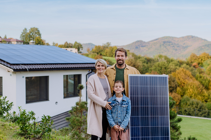 A happy family near their house with solar panel. Alternative energy, saving resources and sustainable lifestyle concept.